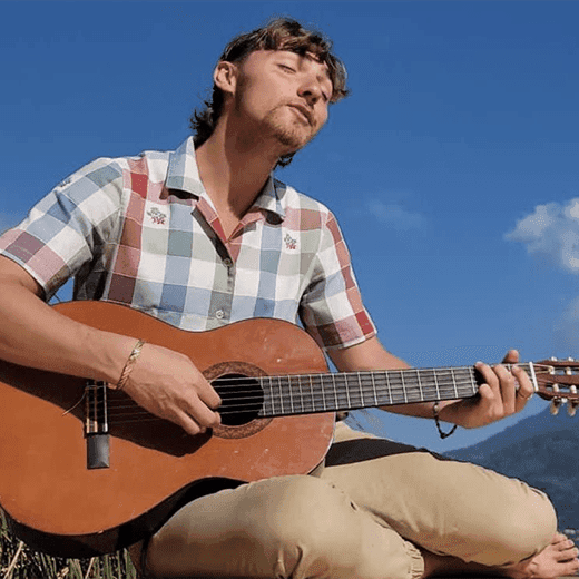 Danny, a HeartSong Mastery student, playing guitar under a blue sky