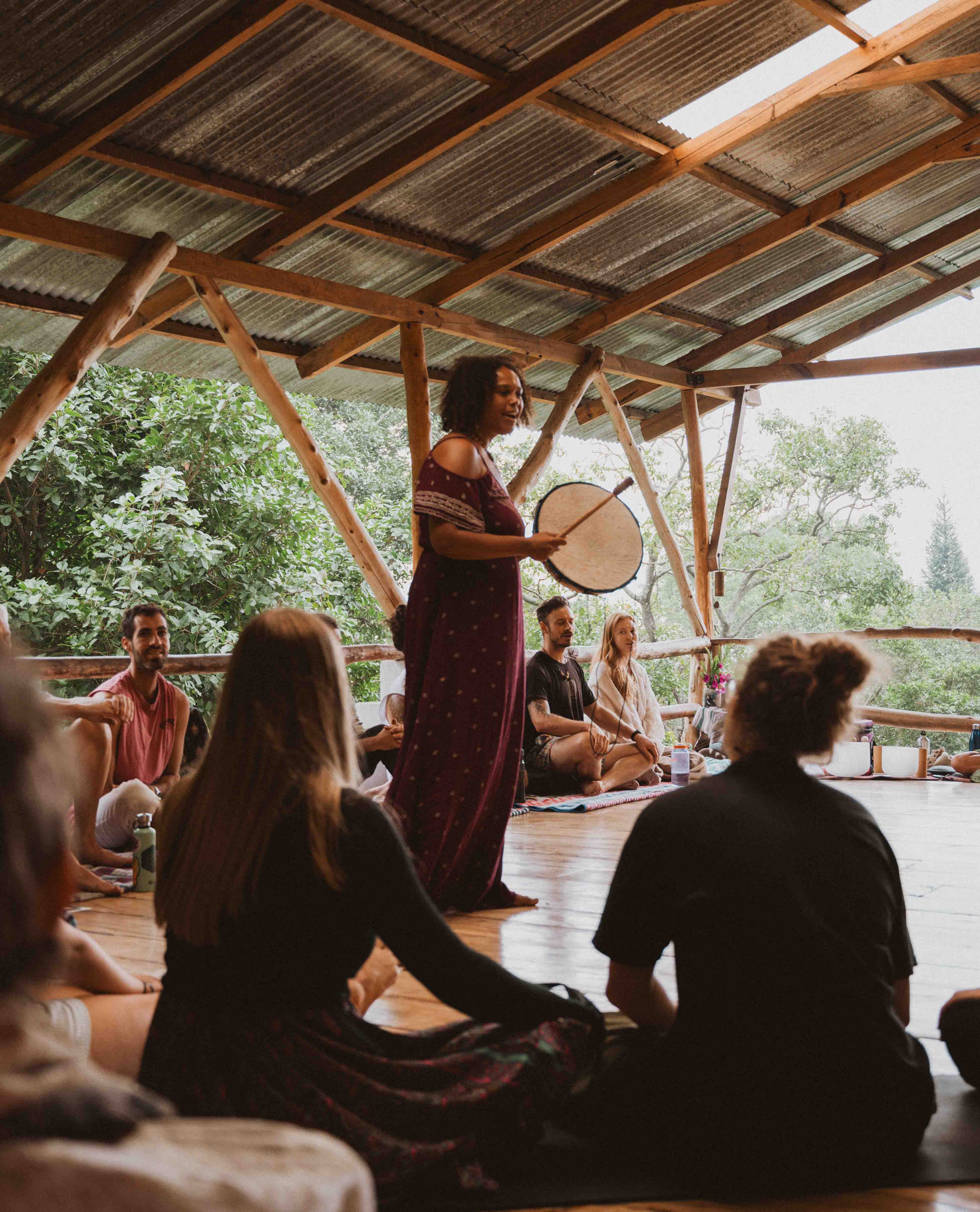 Facilitator holding a frame drum in circle in an open-air shala at Mystical Yoga Farm